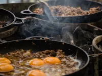 Cast-iron pans of eggs and meat over hot coals